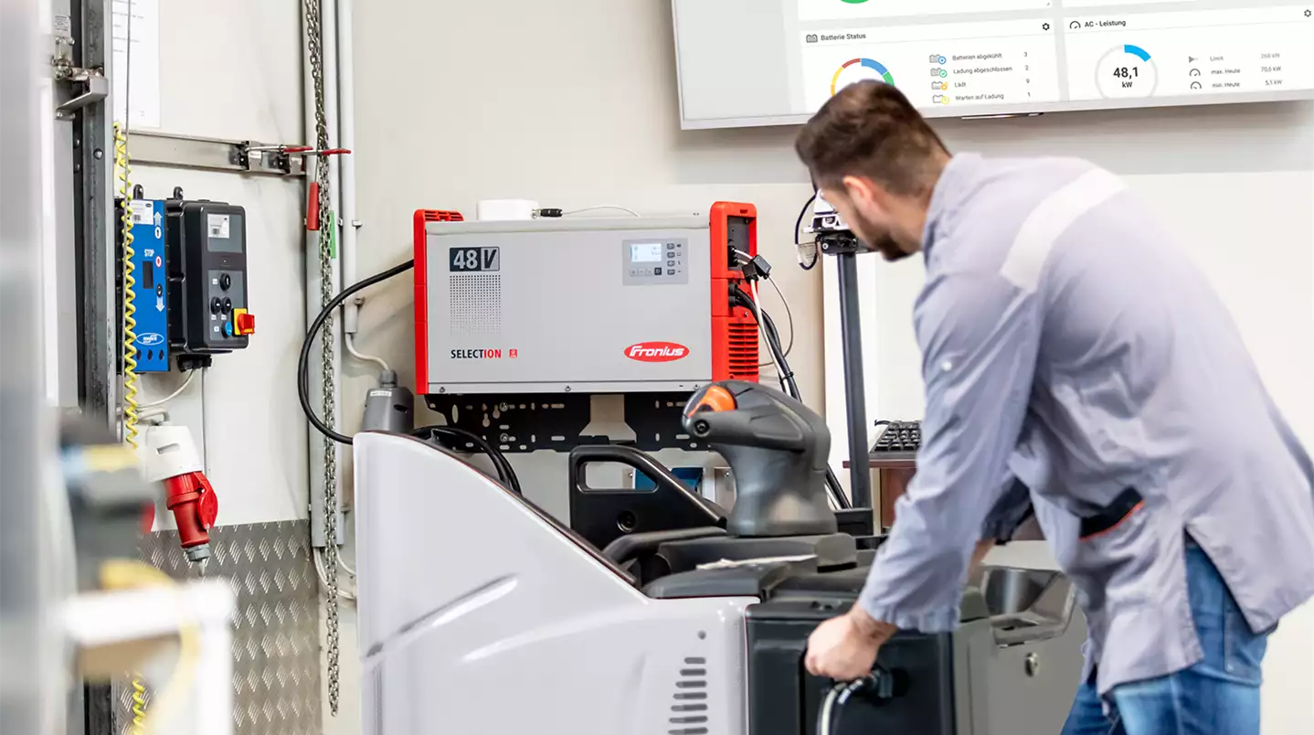 A man is connecting a forklift truck to a SelectION lithium-ion battery charger for charging.