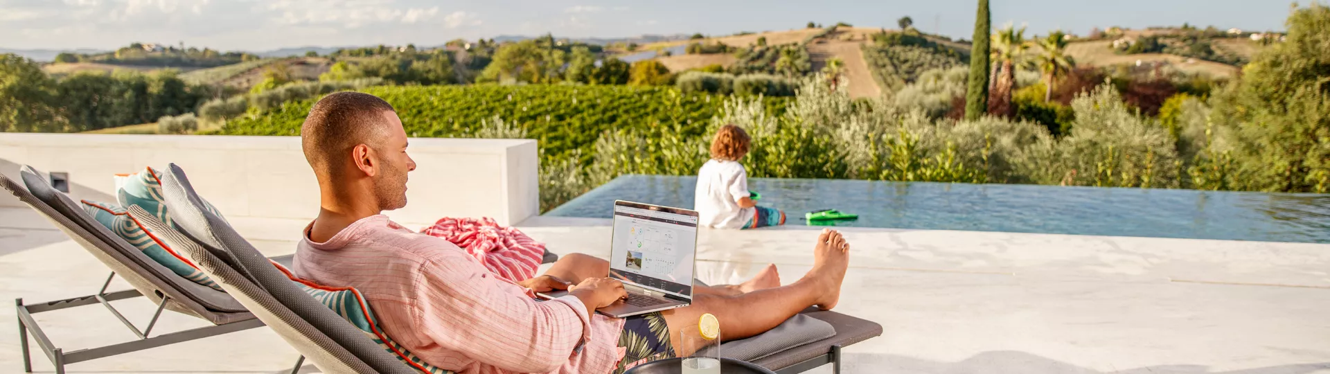 Father monitoring with laptop in front of pool with son